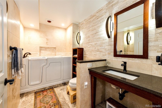 full bathroom with toilet, backsplash, a sink, a garden tub, and tile walls