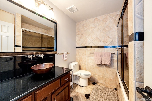 bathroom featuring toilet, tiled shower / bath combo, vanity, visible vents, and tile walls