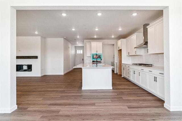25284 E Warren Pl, Aurora, CO 80018 - kitchen with wall chimney range hood, open floor plan, light wood-style floors, recessed lighting, and white cabinetry