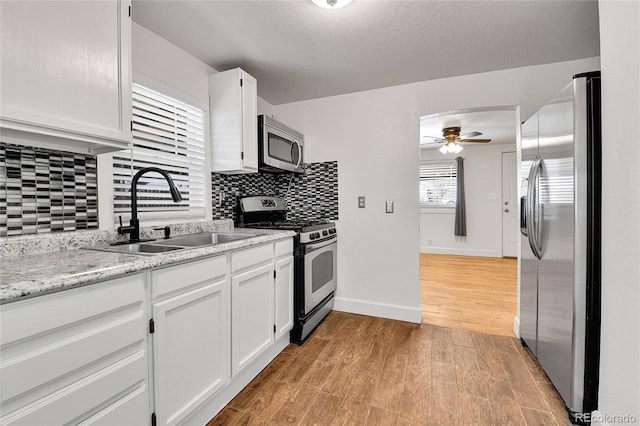 kitchen featuring light wood-type flooring, stainless steel appliances, white cabinetry, a ceiling fan, and a sink