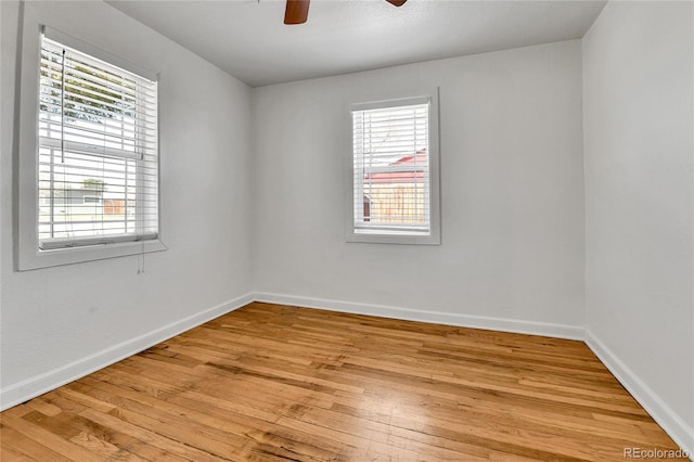 empty room with a wealth of natural light, light wood-type flooring, baseboards, and ceiling fan