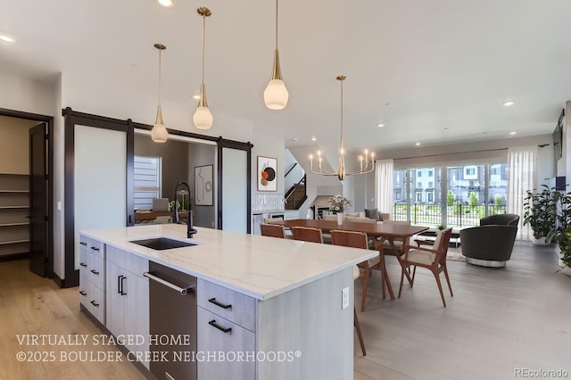 kitchen with a barn door, sink, white cabinetry, hanging light fixtures, and a kitchen island with sink