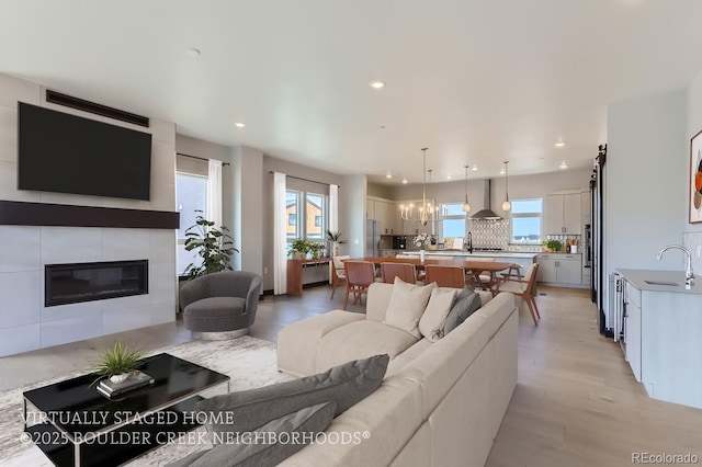 living room featuring light wood-type flooring, a tiled fireplace, plenty of natural light, and sink