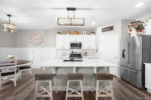 kitchen with an island with sink, sink, white cabinets, hanging light fixtures, and stainless steel appliances