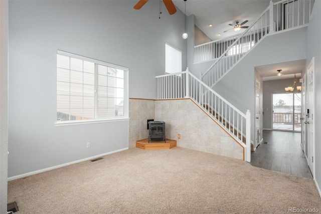 unfurnished living room featuring a towering ceiling, carpet floors, ceiling fan, and a wood stove