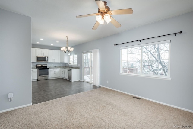 unfurnished living room featuring sink, ceiling fan with notable chandelier, and dark colored carpet