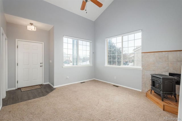 carpeted entryway with lofted ceiling, ceiling fan, and a wood stove