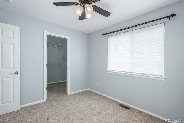 unfurnished bedroom featuring ceiling fan, a spacious closet, light carpet, and a closet