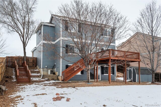 snow covered rear of property with a storage shed and a deck