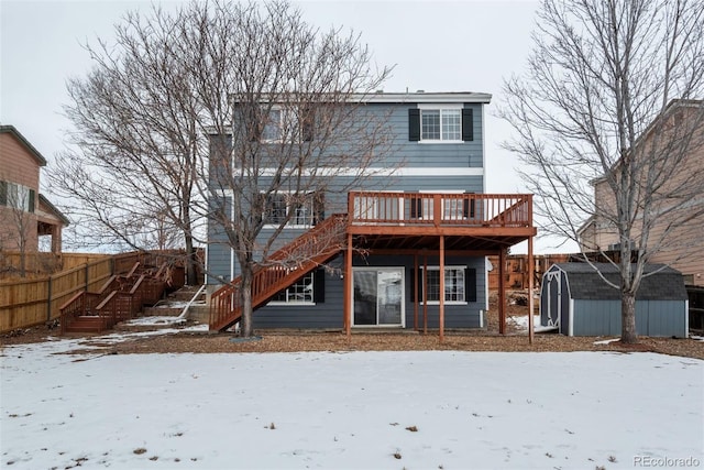 snow covered rear of property with a deck and a storage unit