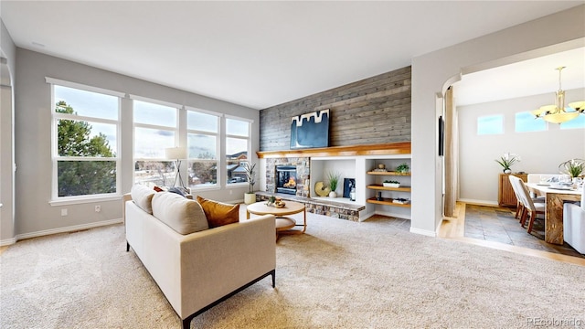 carpeted living room with a notable chandelier, wood walls, and a stone fireplace