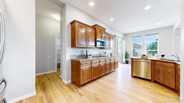 kitchen with light stone countertops, stainless steel appliances, light hardwood / wood-style flooring, and sink