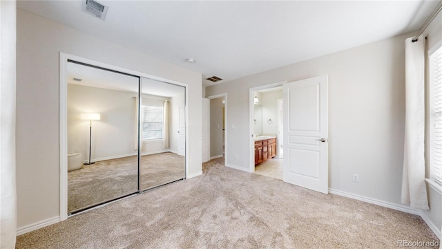 unfurnished bedroom featuring light carpet, ensuite bath, and a closet