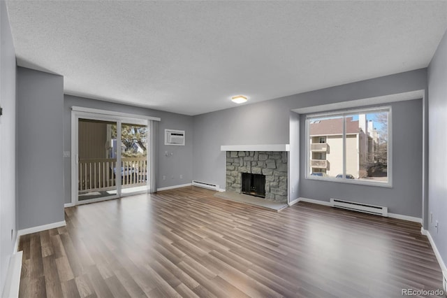 unfurnished living room with baseboard heating, wood finished floors, a fireplace, baseboards, and a textured ceiling