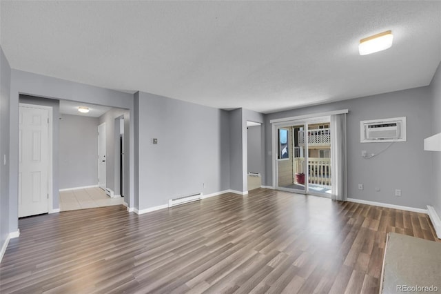 unfurnished living room featuring a wall unit AC, baseboard heating, wood finished floors, baseboards, and a textured ceiling
