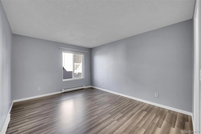 spare room featuring baseboard heating, wood finished floors, a textured ceiling, and baseboards