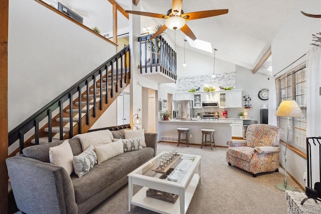 living room featuring a ceiling fan, light colored carpet, high vaulted ceiling, stairs, and beamed ceiling