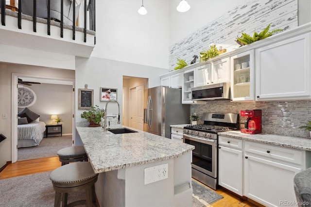 kitchen with appliances with stainless steel finishes, a sink, a towering ceiling, a kitchen breakfast bar, and backsplash