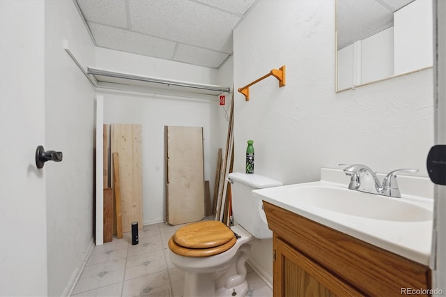 half bathroom featuring toilet, a drop ceiling, baseboards, and vanity