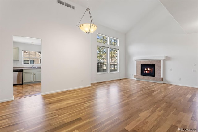 unfurnished living room with a fireplace, light hardwood / wood-style flooring, high vaulted ceiling, and sink