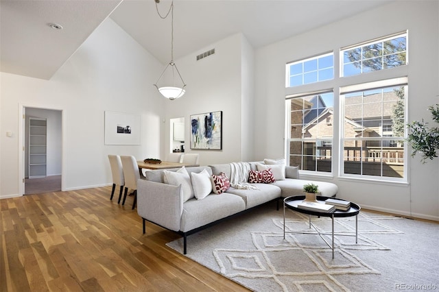 living area featuring high vaulted ceiling, wood finished floors, visible vents, and baseboards