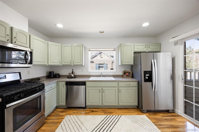 kitchen with stainless steel appliances, light wood-type flooring, green cabinets, a sink, and recessed lighting