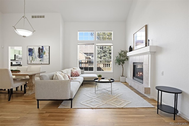 living area featuring a tile fireplace, visible vents, light wood-style flooring, and baseboards