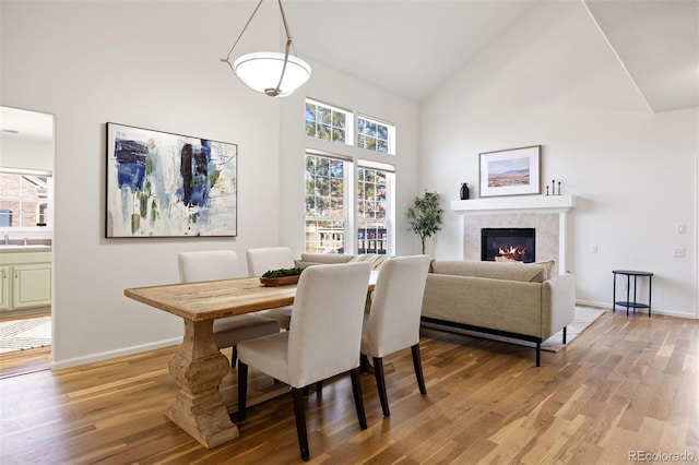 dining space featuring high vaulted ceiling, light wood-style flooring, and baseboards