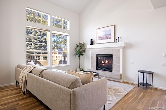 living room with a tile fireplace, vaulted ceiling, baseboards, and wood finished floors