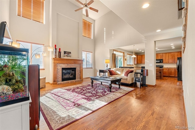 living room featuring ceiling fan, light hardwood / wood-style floors, a towering ceiling, and a brick fireplace