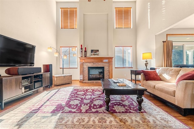 living room with hardwood / wood-style flooring, a towering ceiling, and a brick fireplace