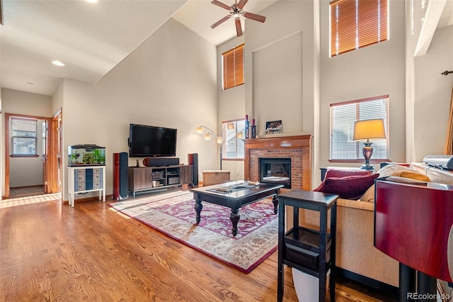 living room with ceiling fan, hardwood / wood-style floors, a high ceiling, and a brick fireplace