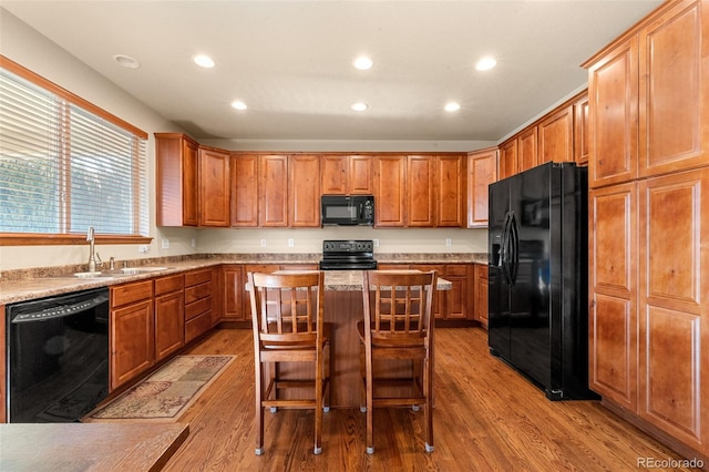 kitchen with a breakfast bar, sink, black appliances, light hardwood / wood-style flooring, and a center island