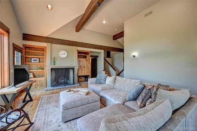 living room with vaulted ceiling with beams, light wood-type flooring, a brick fireplace, and built in shelves