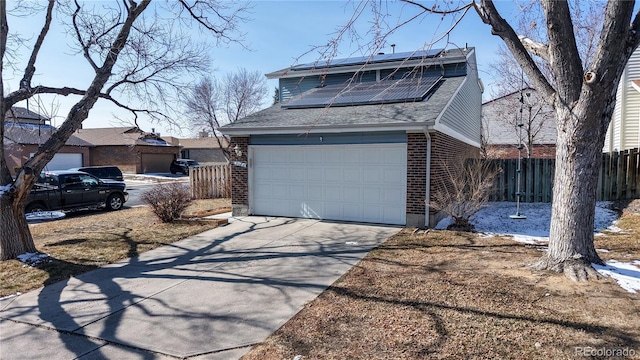 view of front of house with concrete driveway, an attached garage, fence, roof mounted solar panels, and brick siding