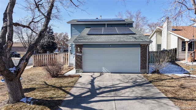 view of front facade with a garage, solar panels, brick siding, and fence