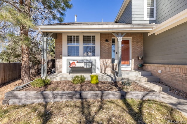 entrance to property featuring a porch, brick siding, and fence