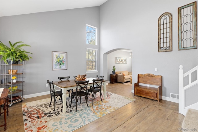 dining room with arched walkways, high vaulted ceiling, visible vents, baseboards, and light wood finished floors