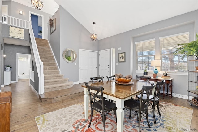 dining space with high vaulted ceiling, baseboards, stairway, and wood finished floors