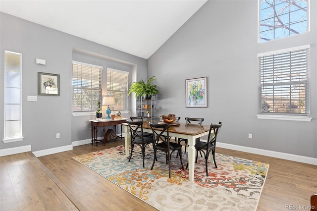 dining room with high vaulted ceiling, baseboards, and wood finished floors