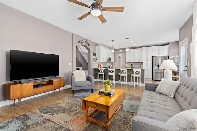 living room featuring arched walkways, light wood finished floors, recessed lighting, a ceiling fan, and baseboards