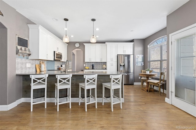 kitchen featuring arched walkways, stainless steel appliances, tasteful backsplash, a sink, and a peninsula