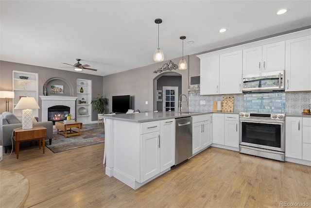 kitchen featuring a peninsula, a fireplace, a sink, open floor plan, and appliances with stainless steel finishes