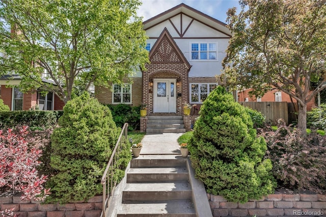 tudor-style house with brick siding, fence, and stucco siding