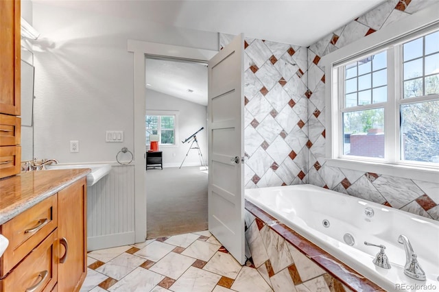 full bath with baseboards, a tub with jets, lofted ceiling, and vanity