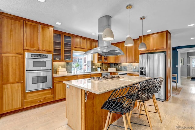 kitchen with a kitchen breakfast bar, appliances with stainless steel finishes, island range hood, and light wood-type flooring