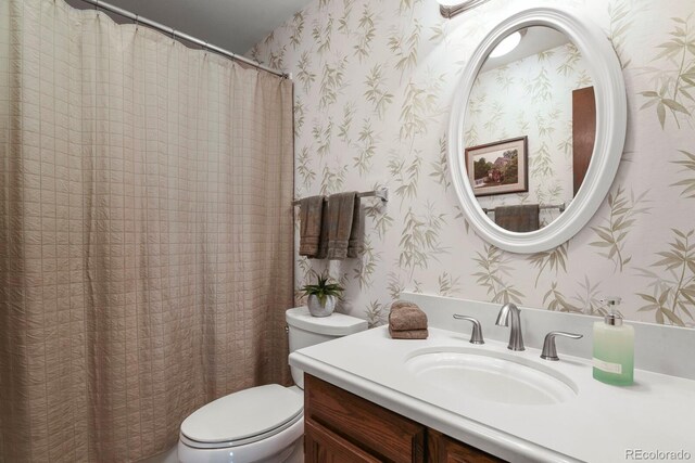 bathroom with vanity, toilet, and wallpapered walls