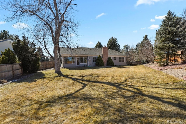 view of front of home with a front yard, a fenced backyard, and a chimney