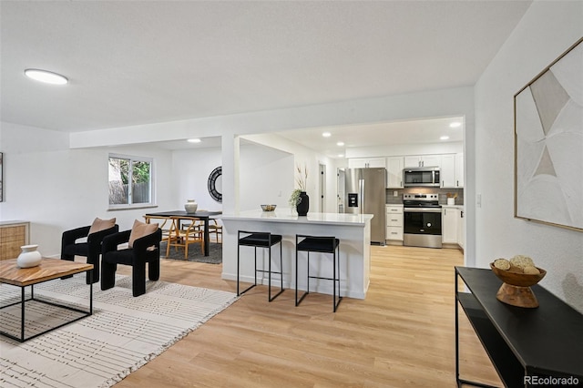 11176 W 62nd Ave, Arvada, CO 80004 - kitchen with stainless steel appliances, white cabinetry, light wood finished floors, a breakfast bar, and a peninsula