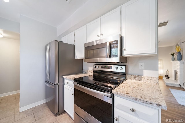 kitchen featuring light stone counters, stainless steel appliances, a brick fireplace, and white cabinets